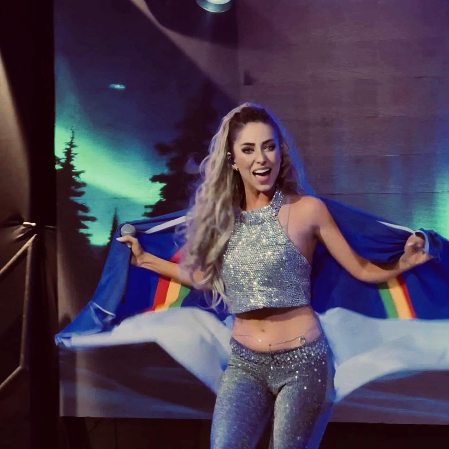 Jessy Portilla segurando bandeira colorida no palco, performance intensa