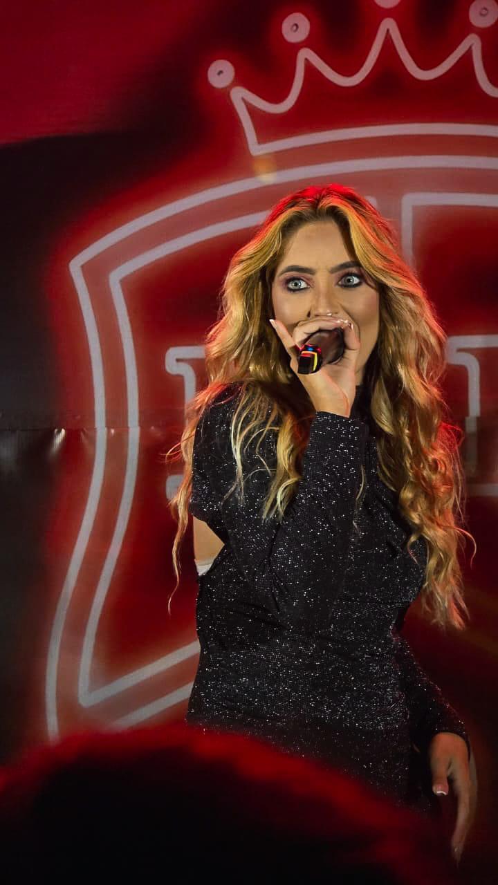 Jessy Portilla no palco, look preto com brilho, microfone na mão
