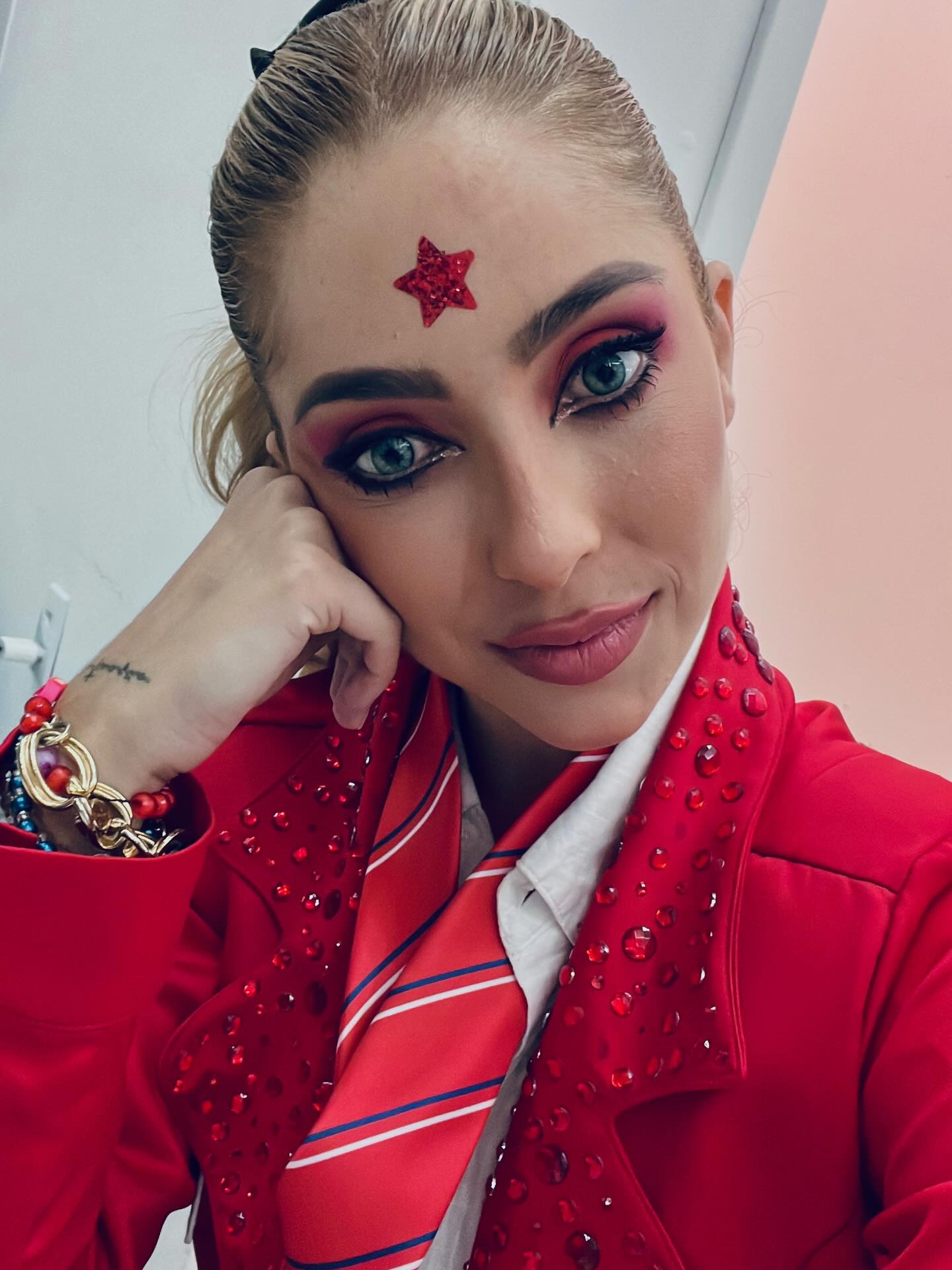 Jessy Portilla com blazer vermelho de brilho, gravata e estrela na testa